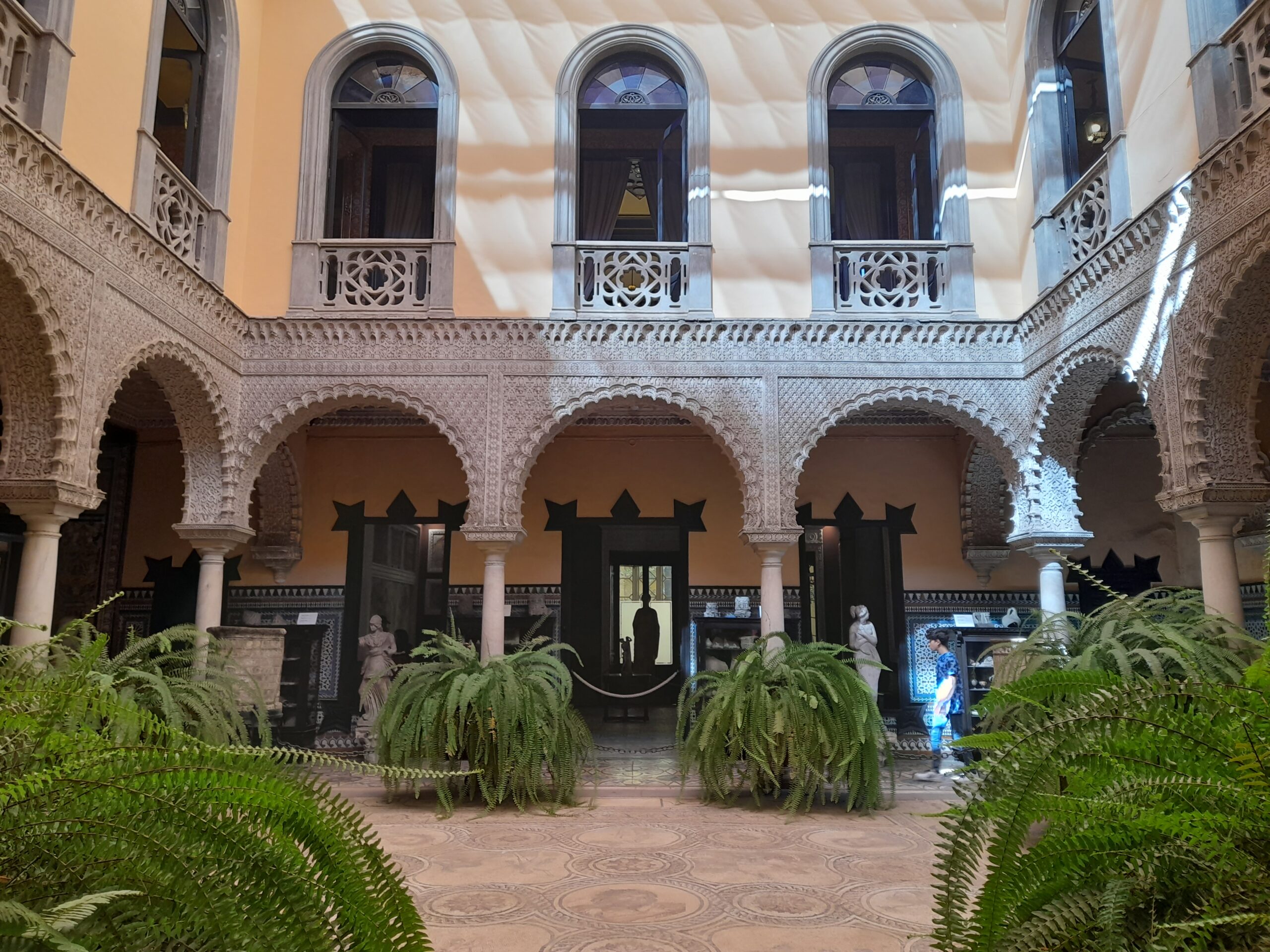 Patio del Palacio de la Condesa de Lebrija en Sevilla con arcos, mosaicos en el suelo y estatuas romanas al fondo, foto de Conoce Sevilla