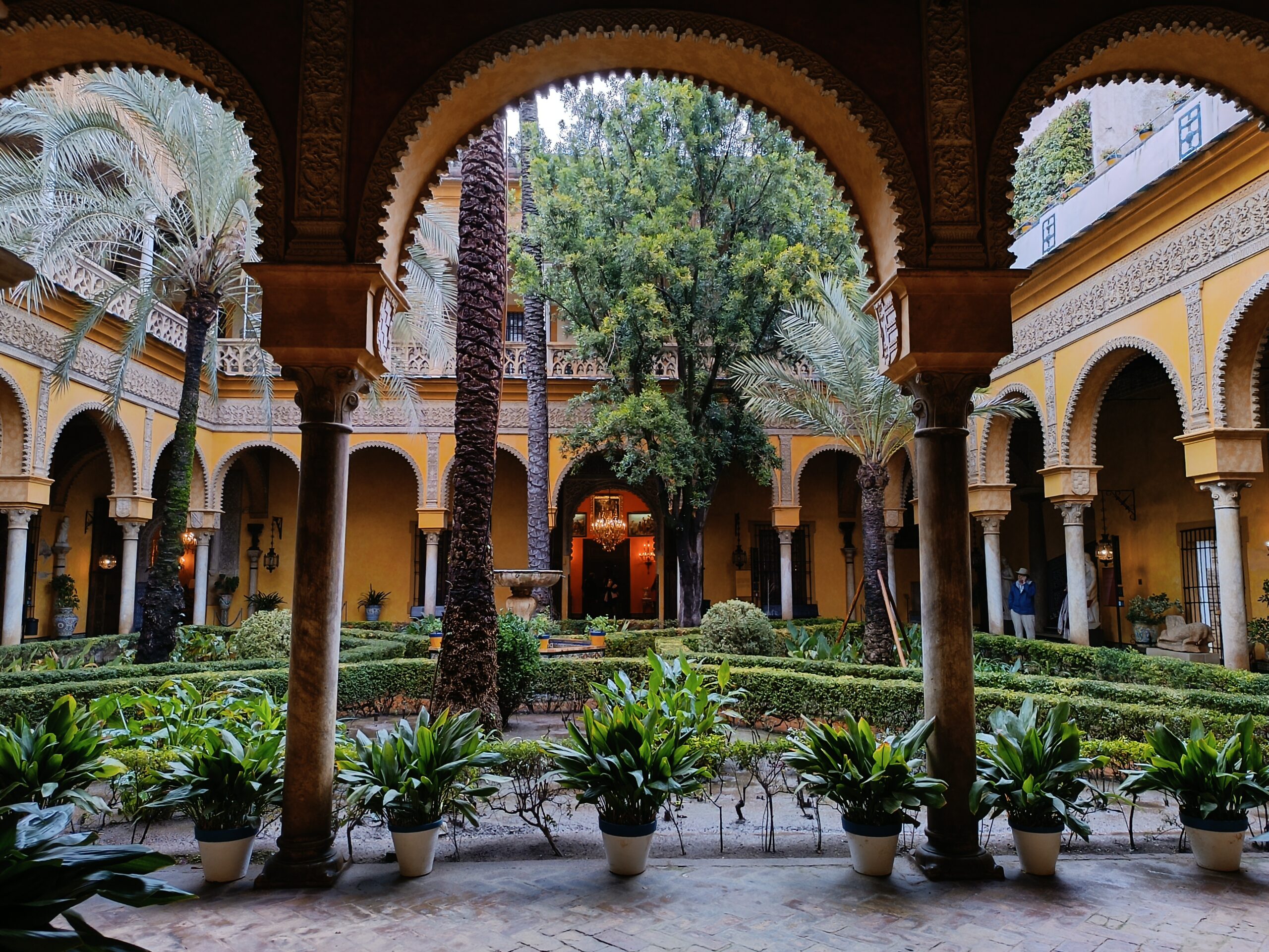 Patio del Palacio de Dueñas en Sevilla con arcada central, fuente al fondo y vegetación a los lados, foto de Conoce Sevilla