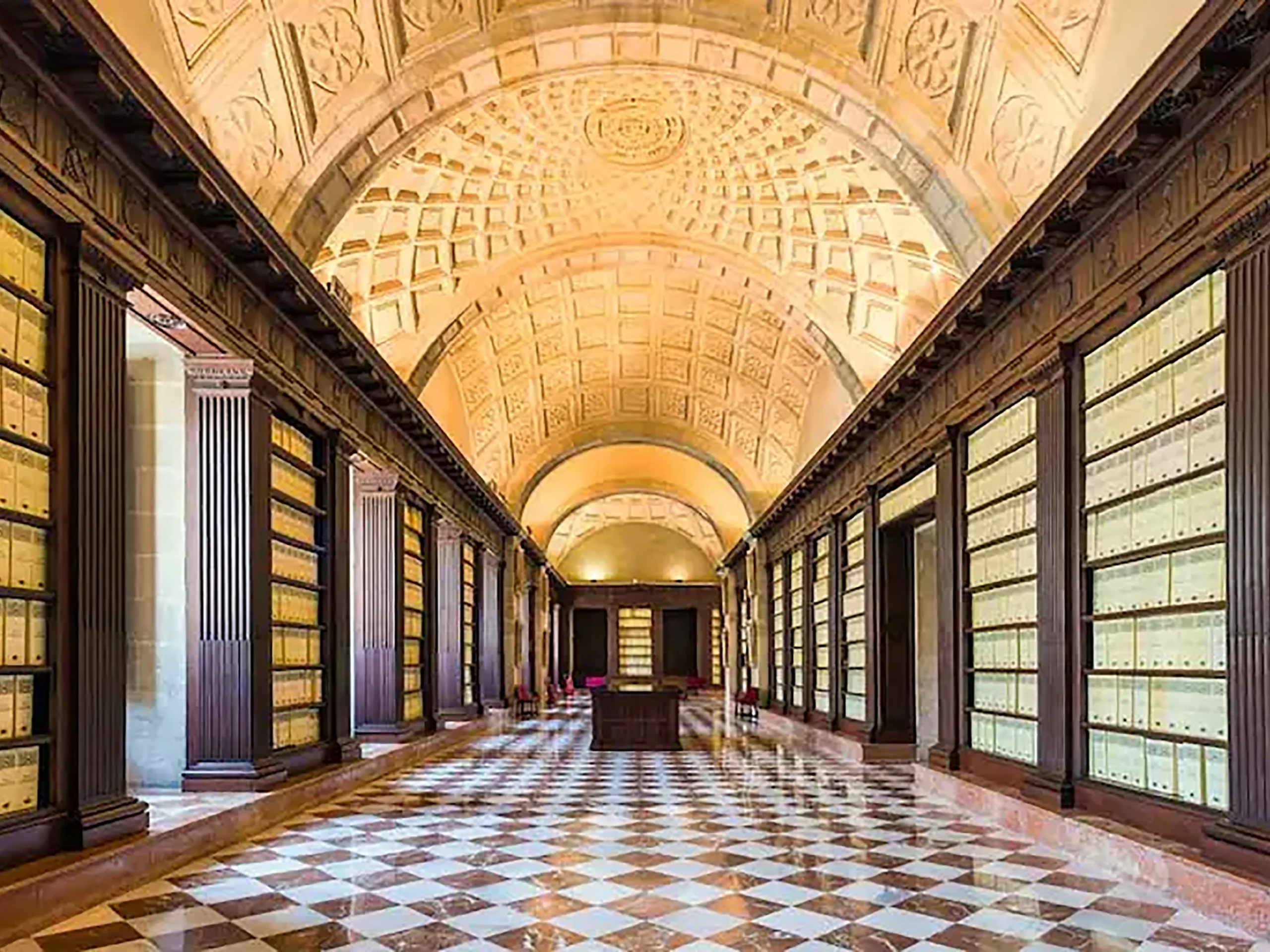 Interior del Archivo de Indias en Sevilla con estanterías llenas de tomos y bóveda del techo durante una visita cultural con Conoce Sevilla