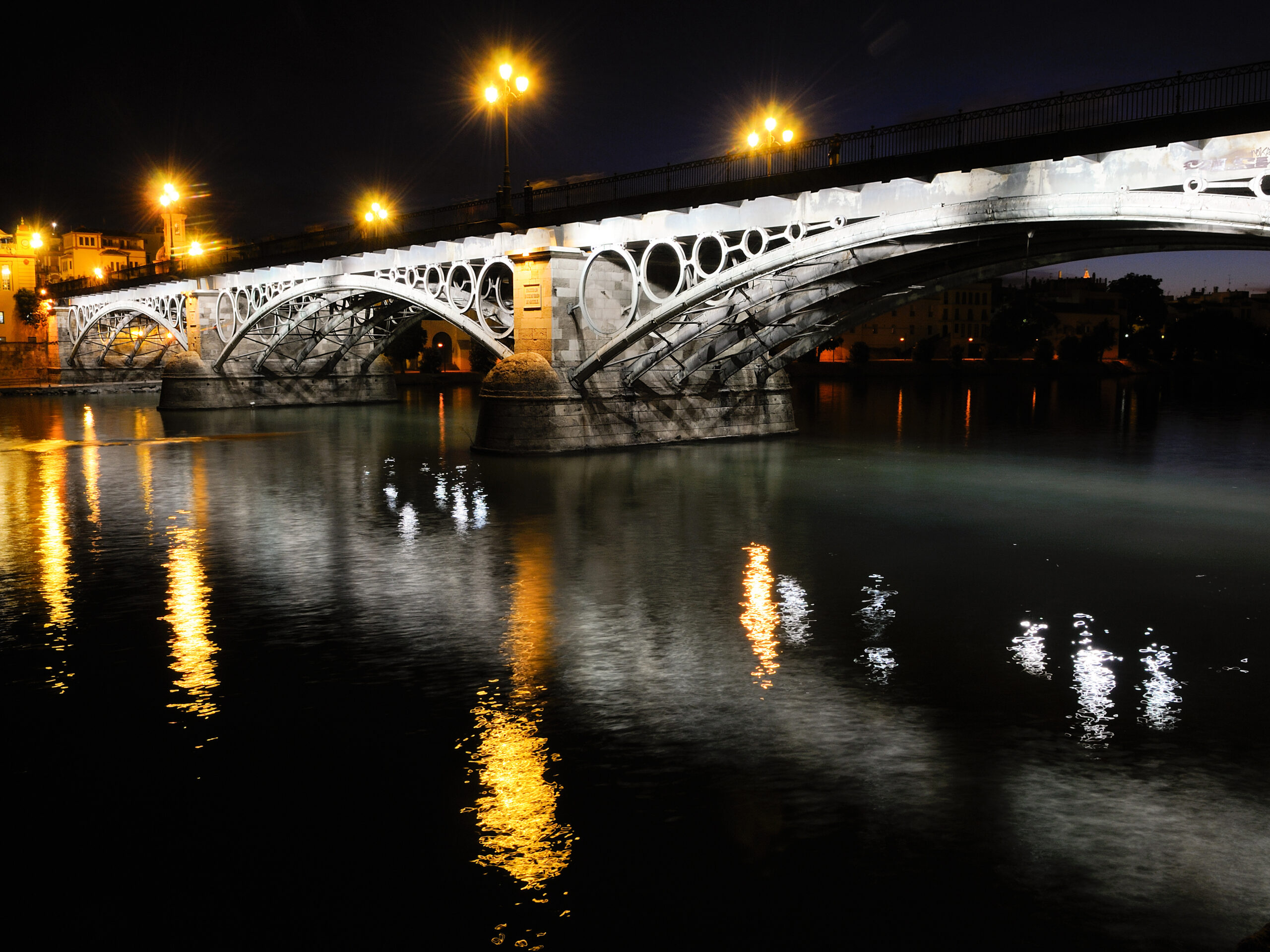 Puente de Triana o Isabel II sobre el río Guadalquivir de noche durante una visita cultural con Conoce Sevilla